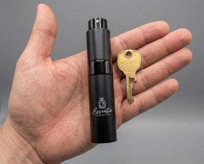 Hand holding a black essential oil diffuser labeled 'Essentia' with a key for scale on a gray background.