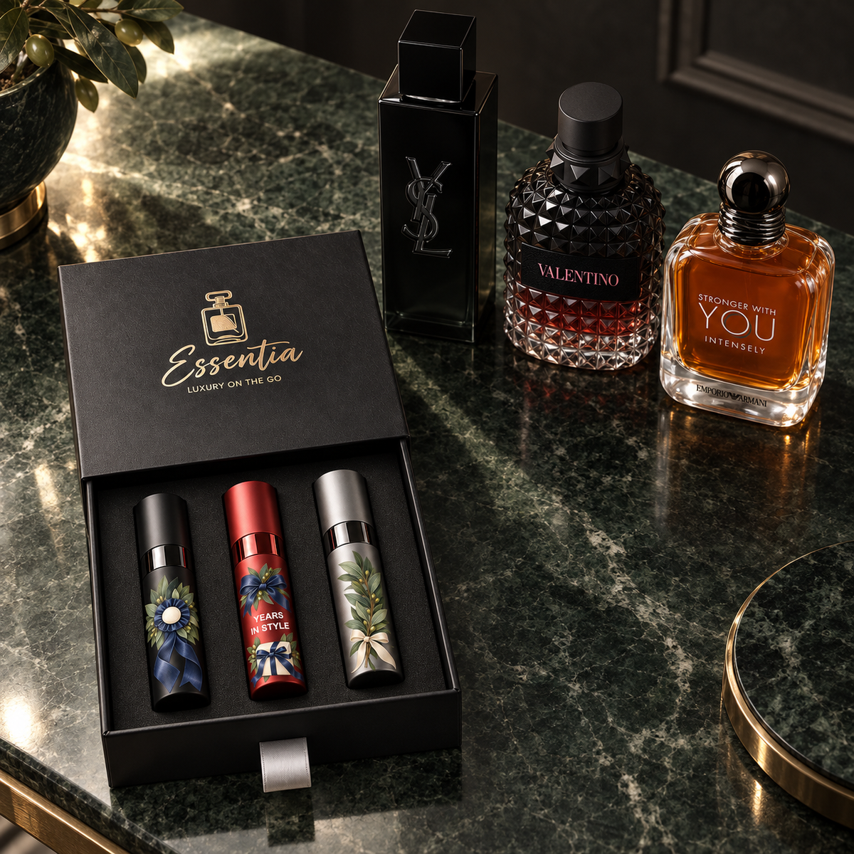 Essentia The Milestone Trio — For Him: 3 decorated 10ml atomizers (black, red, silver) in a black gift box, with the corresponding full-size fragrance bottles behind.